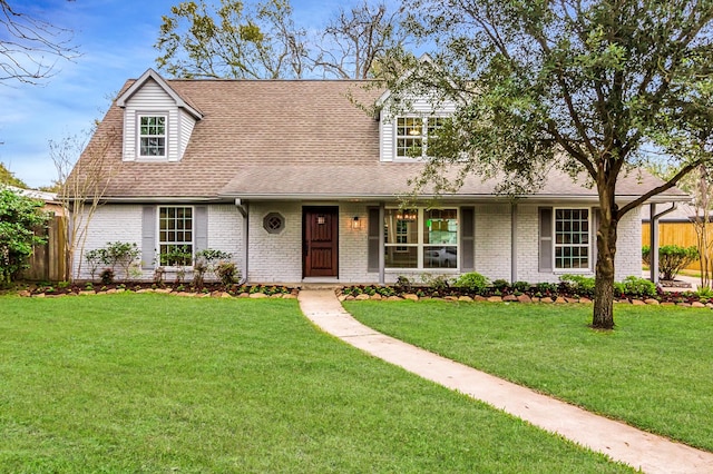 view of front of property featuring a shingled roof, brick siding, fence, and a front lawn