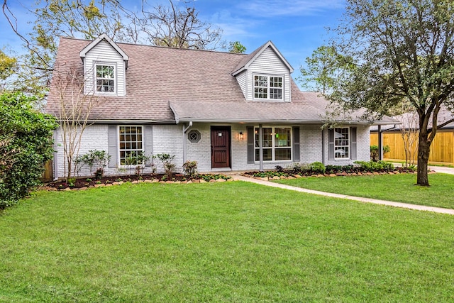 new england style home featuring roof with shingles, fence, a front lawn, and brick siding