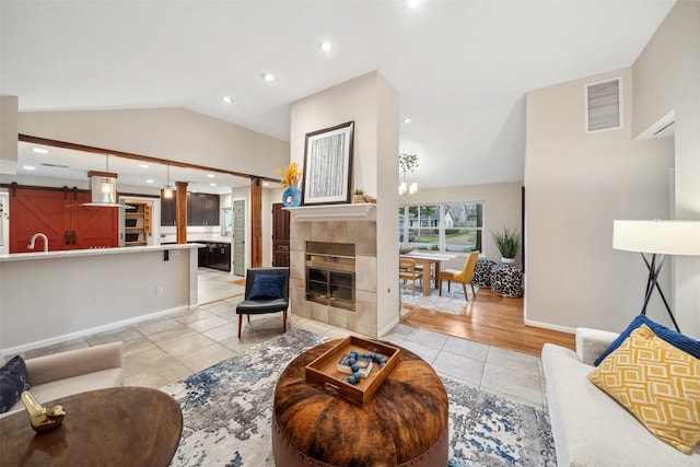 living area featuring light tile patterned floors, lofted ceiling, visible vents, a barn door, and a tile fireplace