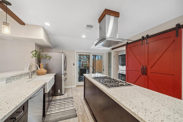 kitchen with pendant lighting, stacked washer and clothes dryer, island exhaust hood, stainless steel appliances, and visible vents