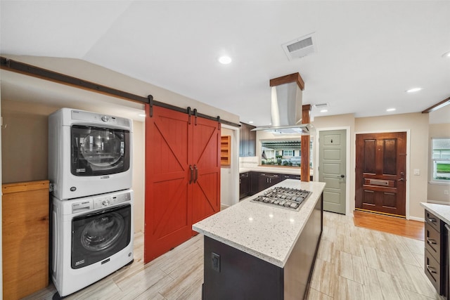 kitchen with a barn door, island range hood, stacked washer / dryer, a center island, and stainless steel gas cooktop