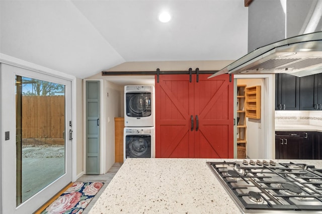 kitchen featuring stacked washer / dryer, stainless steel gas stovetop, lofted ceiling, and light stone countertops