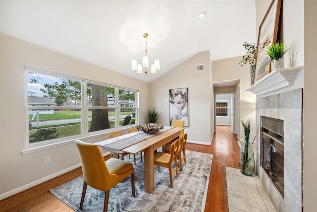 dining area with lofted ceiling, baseboards, a tiled fireplace, and light wood finished floors