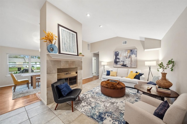 living room with light tile patterned floors, visible vents, baseboards, vaulted ceiling, and a tiled fireplace