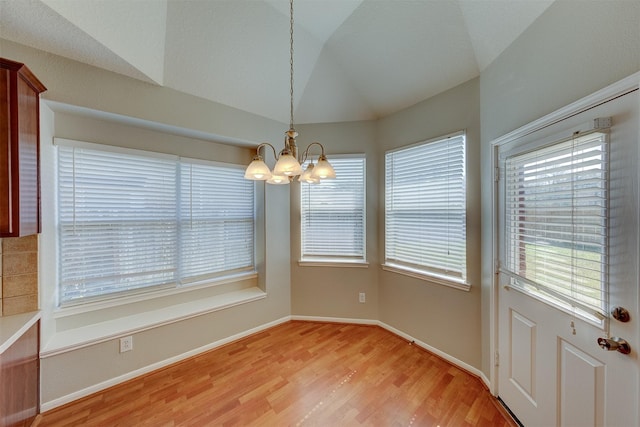 unfurnished dining area with lofted ceiling, a healthy amount of sunlight, light wood-type flooring, and an inviting chandelier