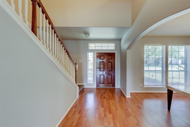 entryway featuring light wood-style floors, stairs, baseboards, and arched walkways