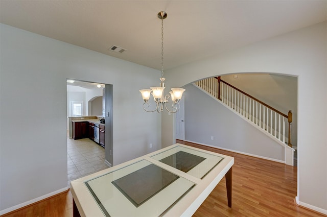 dining space with arched walkways, light wood finished floors, visible vents, stairway, and baseboards