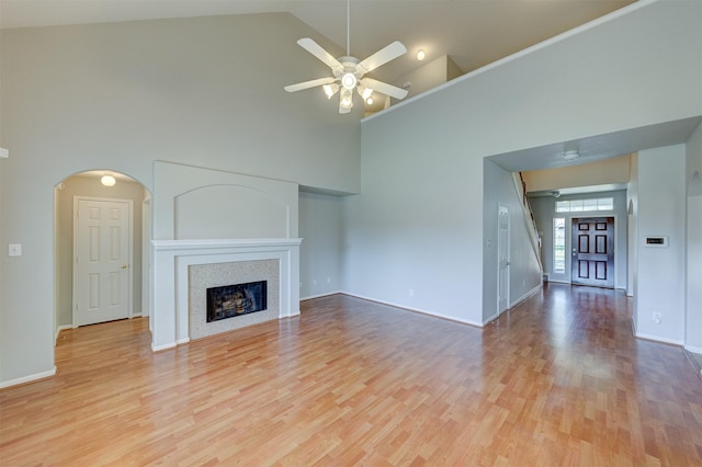 unfurnished living room with arched walkways, high vaulted ceiling, light wood finished floors, and a fireplace