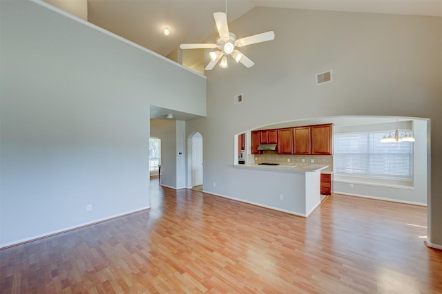 unfurnished living room featuring light wood-style floors, visible vents, arched walkways, and ceiling fan with notable chandelier