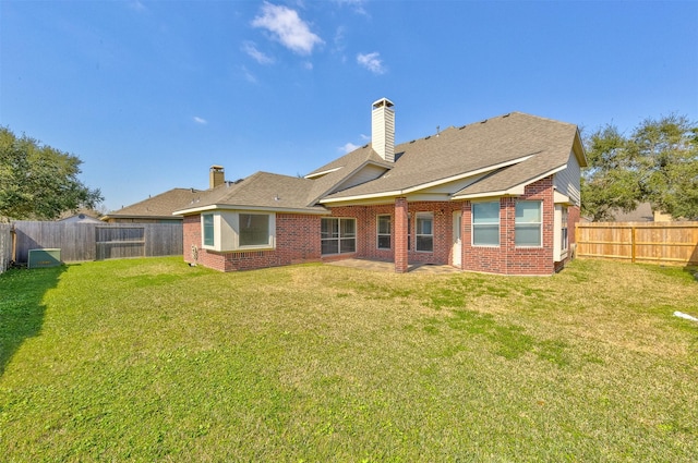 back of property featuring a yard, brick siding, a chimney, and a fenced backyard