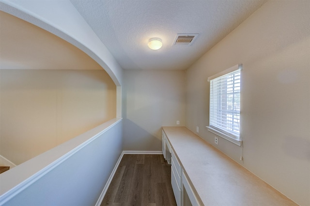 hall featuring baseboards, a textured ceiling, visible vents, and dark wood-type flooring