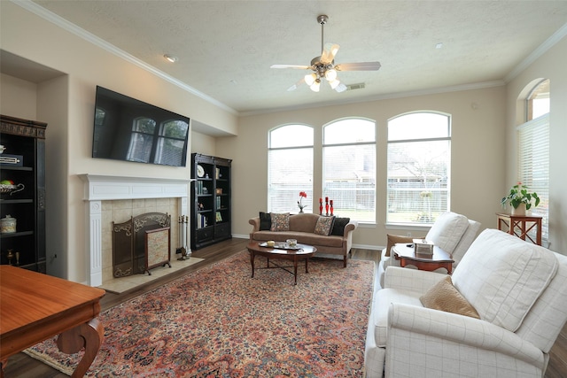 living room featuring visible vents, ornamental molding, a tile fireplace, wood finished floors, and a textured ceiling