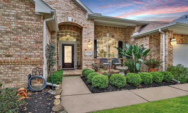 exterior entry at dusk featuring a garage and brick siding