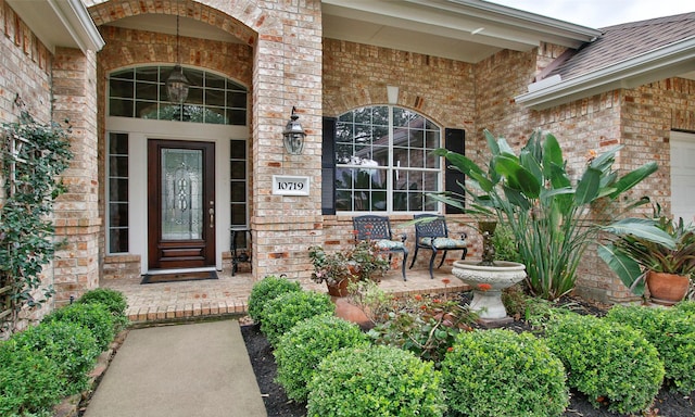 property entrance with covered porch, brick siding, and a shingled roof