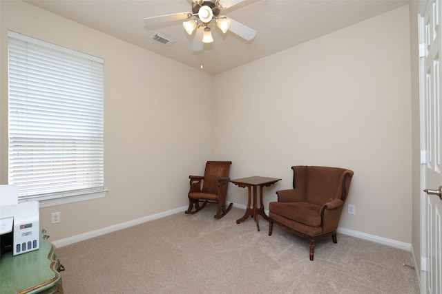 living area featuring visible vents, light colored carpet, baseboards, and ceiling fan