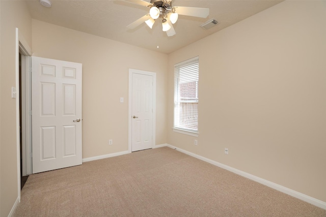 unfurnished bedroom featuring light carpet, visible vents, a ceiling fan, and baseboards