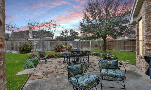 patio terrace at dusk featuring a yard and a fenced backyard