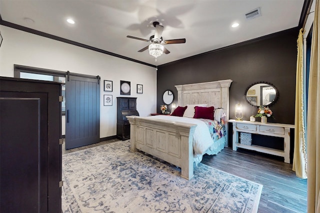 bedroom featuring a barn door, wood finished floors, visible vents, baseboards, and crown molding