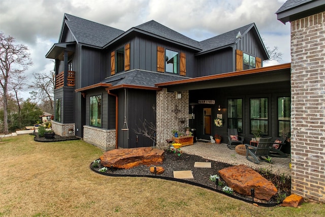 view of front of home featuring board and batten siding, a front yard, brick siding, and a shingled roof