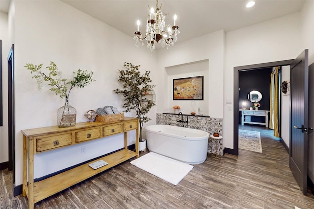 bathroom with a soaking tub, a notable chandelier, baseboards, and wood finished floors