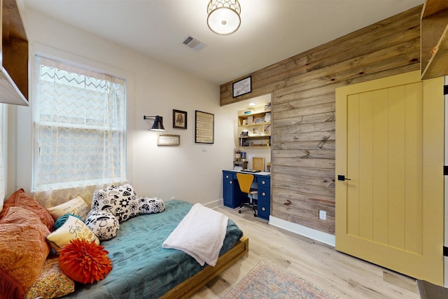 bedroom with baseboards, light wood finished floors, visible vents, and wooden walls