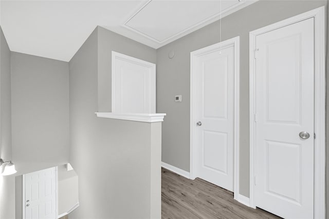 corridor featuring light wood-style flooring, attic access, and baseboards