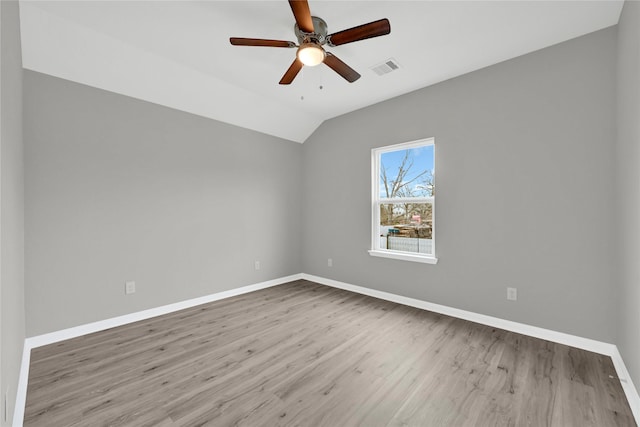 empty room with visible vents, light wood-style floors, vaulted ceiling, a ceiling fan, and baseboards