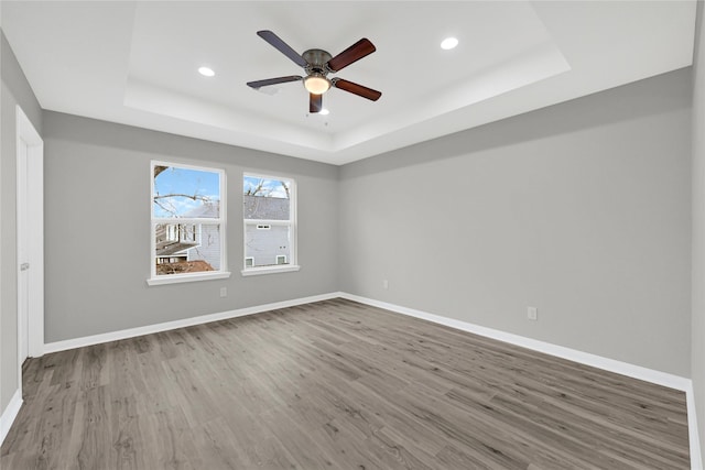 empty room with a tray ceiling, baseboards, and wood finished floors