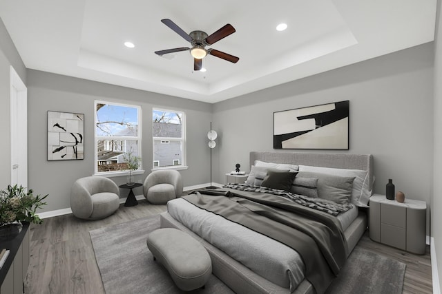 bedroom with baseboards, a tray ceiling, wood finished floors, and recessed lighting