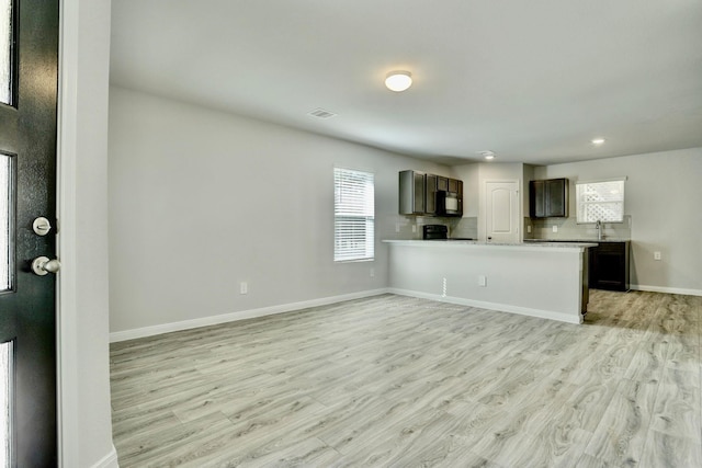 kitchen featuring open floor plan, a peninsula, light countertops, light wood-type flooring, and black microwave