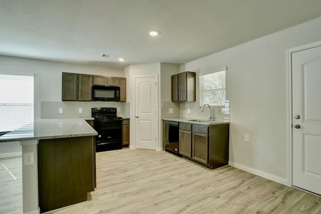 kitchen with light wood finished floors, visible vents, black appliances, light stone countertops, and a kitchen breakfast bar