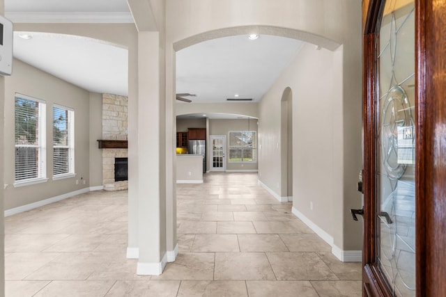 foyer featuring arched walkways, a fireplace, baseboards, and a ceiling fan