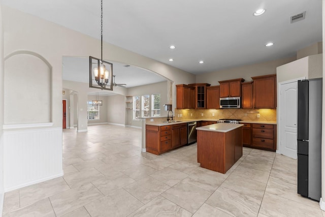 kitchen with a sink, a kitchen island, a chandelier, brown cabinets, and stainless steel appliances