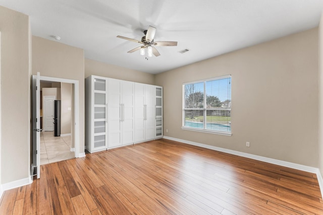 unfurnished bedroom featuring freestanding refrigerator, baseboards, light wood finished floors, and visible vents