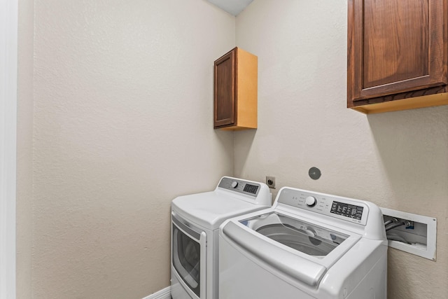 washroom with baseboards, cabinet space, a textured wall, and washer and clothes dryer