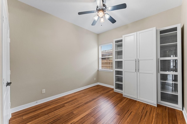 unfurnished bedroom featuring baseboards, dark wood-style flooring, and a ceiling fan