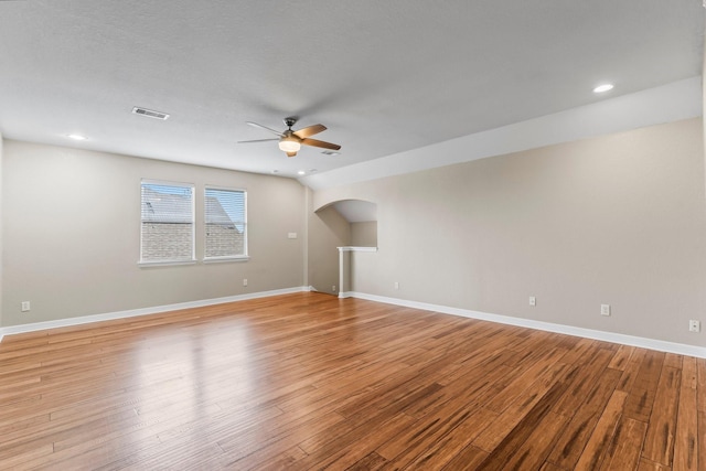 empty room with baseboards, arched walkways, light wood-style floors, visible vents, and ceiling fan