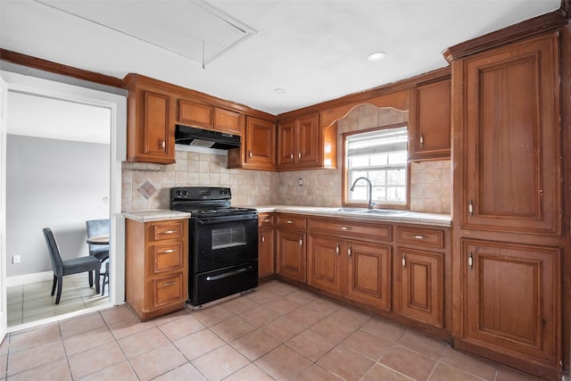 kitchen featuring black electric range, light countertops, decorative backsplash, brown cabinetry, and under cabinet range hood