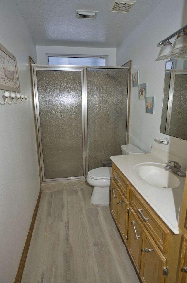 bathroom featuring a stall shower, visible vents, toilet, wood finished floors, and vanity