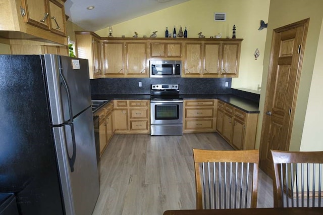 kitchen featuring visible vents, light wood-style floors, vaulted ceiling, appliances with stainless steel finishes, and dark countertops