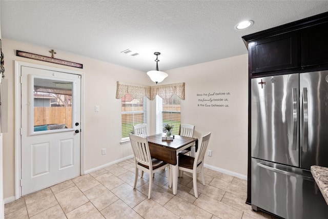 dining area with a textured ceiling, light tile patterned flooring, visible vents, and baseboards