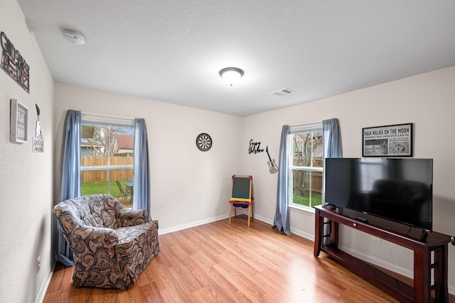 sitting room featuring visible vents, light wood-style flooring, baseboards, and a textured ceiling