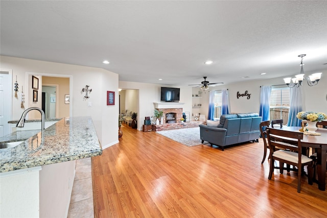 living area featuring light wood-style floors, recessed lighting, a fireplace, and ceiling fan with notable chandelier