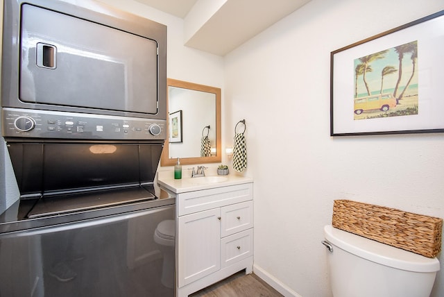 laundry area featuring a sink, stacked washing maching and dryer, wood finished floors, laundry area, and baseboards