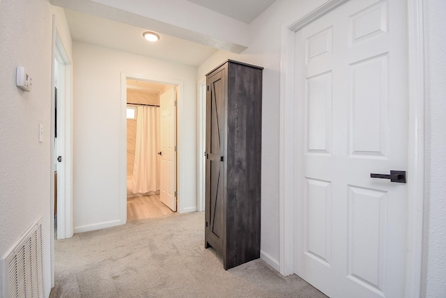 hallway with visible vents, light carpet, and baseboards