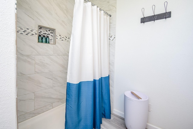 bathroom featuring baseboards, a tile shower, and wood finished floors