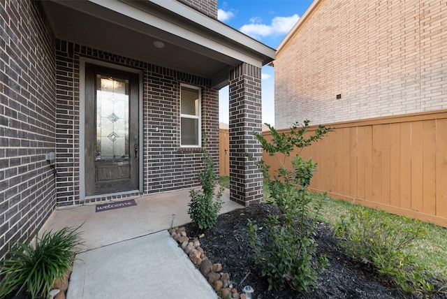 view of exterior entry featuring fence and brick siding