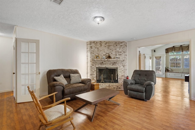 living area featuring a brick fireplace, visible vents, a textured ceiling, and wood finished floors