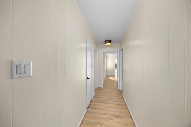 hall featuring light wood-style floors, crown molding, and baseboards