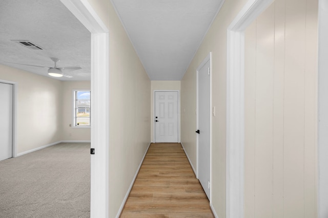 corridor with baseboards, visible vents, a textured ceiling, and light colored carpet